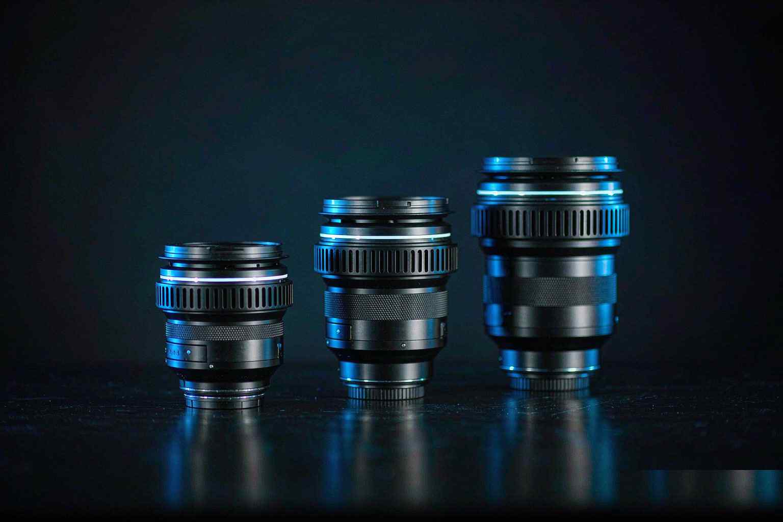 Três lentes fotográficas dispostas em ordem crescente sobre uma superfície escura, com luz de contorno azul fria, simbolizando o acúmulo de especificações nos modelos de vídeo