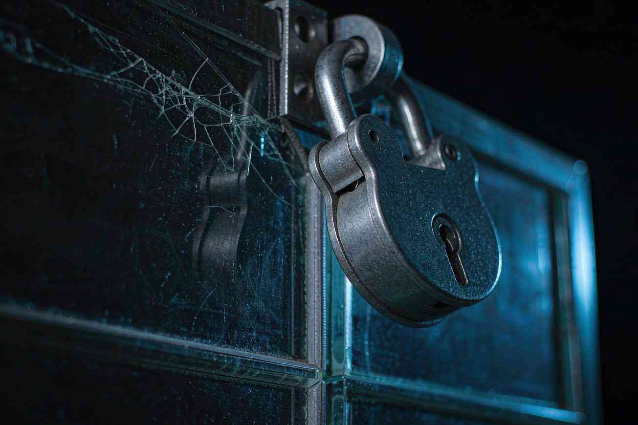 Un candado de metal pesado sobre un panel de vidrio agrietado bajo una luz azul fría, evocando un límite de confianza roto en un canal de seguridad
