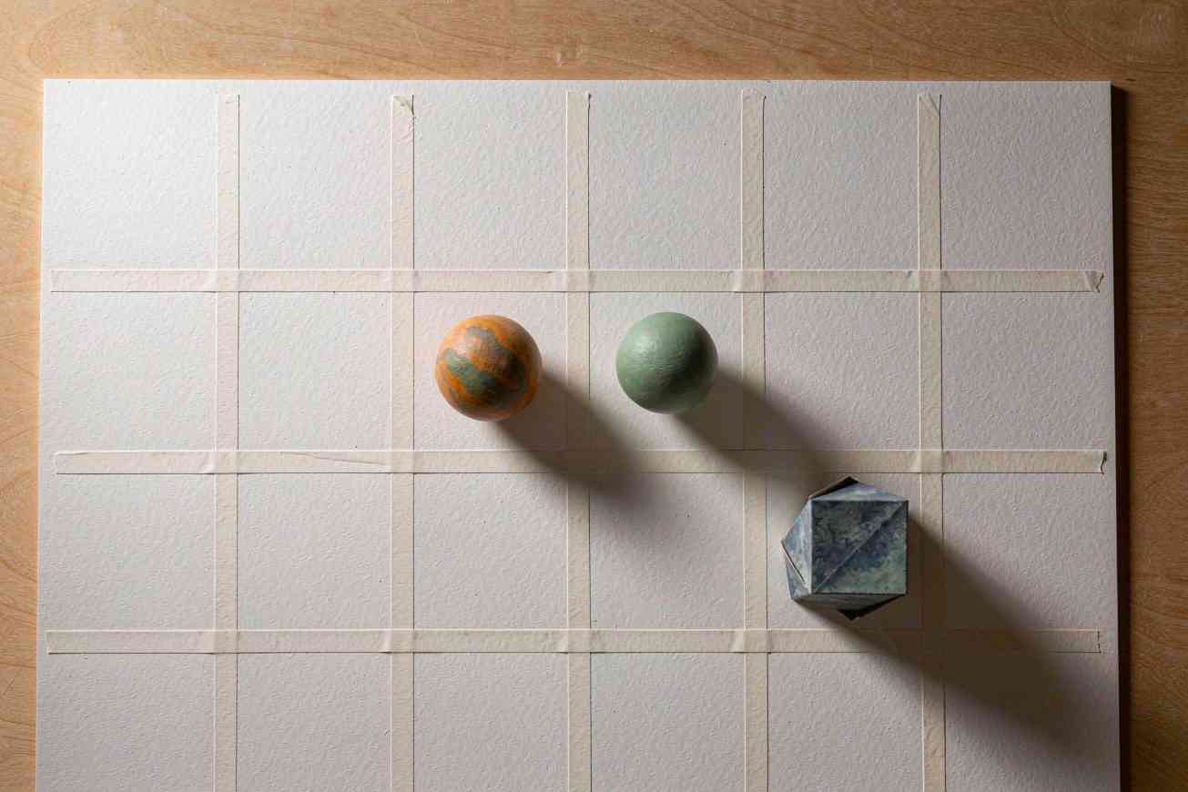 A blank sheet of paper taped into an even grid on a wooden desk, with a few small abstract objects resting in some of the squares