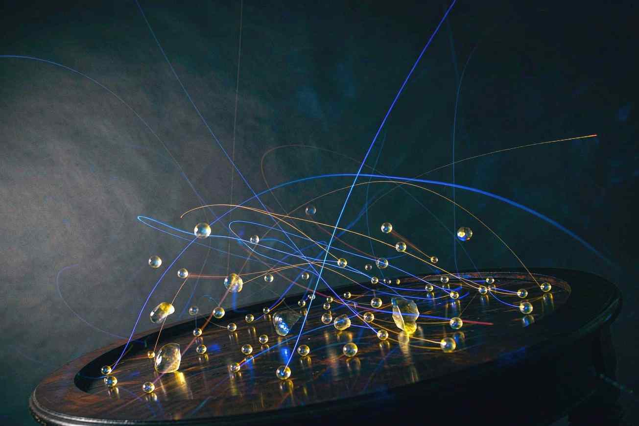 A dark round table seen from a low angle, dozens of small glowing pieces caught mid-motion with thin lines of light tracing their paths