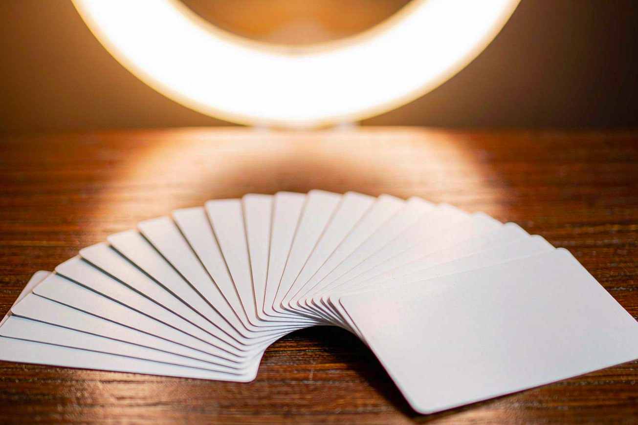A neat fan of blank matte white cards spread across a warm wooden desk under a softly blurred ring light