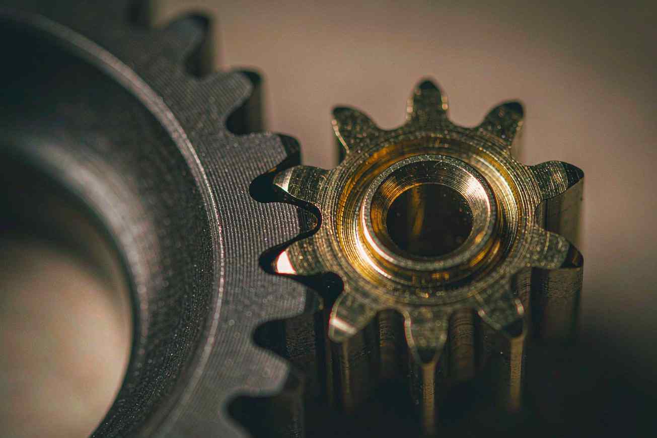 A small brass gear meshing precisely into a much larger dark steel gear under warm directional light