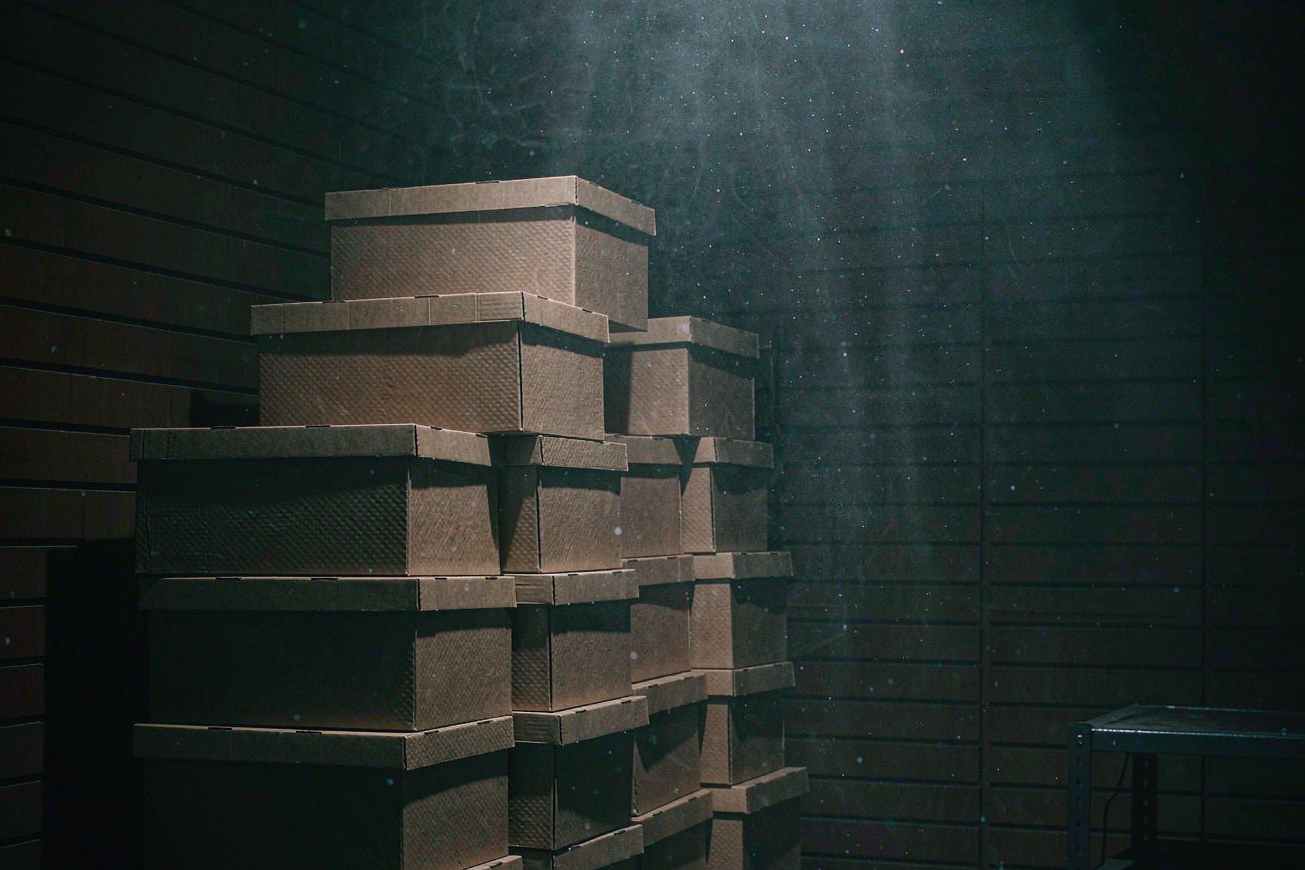 Una pila alta di scatole d'archivio semplici e sigillate in un magazzino buio sotto un raggio di luce fredda