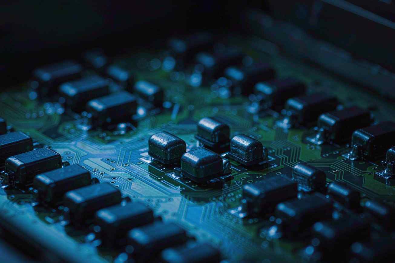 A green circuit board on a dark surface, with cool blue light sweeping across neatly arranged black chips