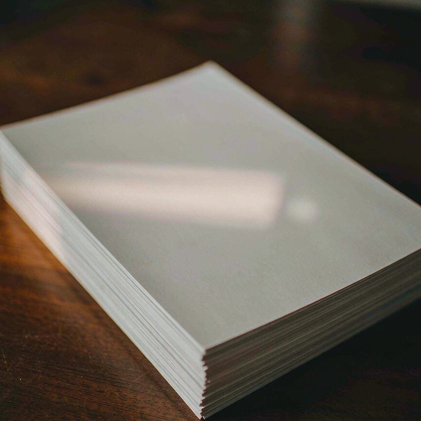 Ein dicker Stapel leerer weißer Fotoprints auf einem dunklen Holztisch
