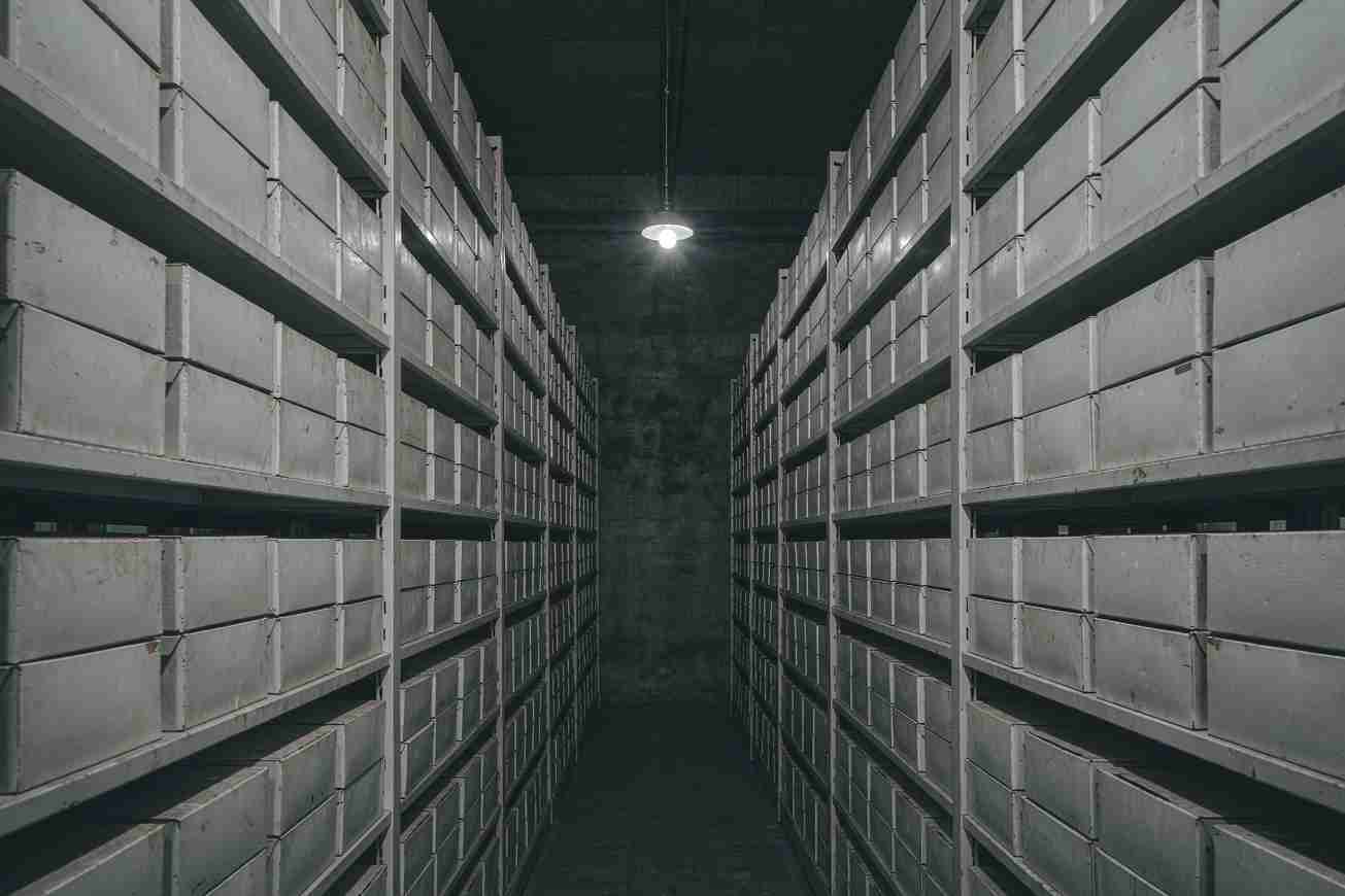 Une allée d'archives souterraine et sombre bordée d'étagères métalliques remplies de boîtes de stockage grises
