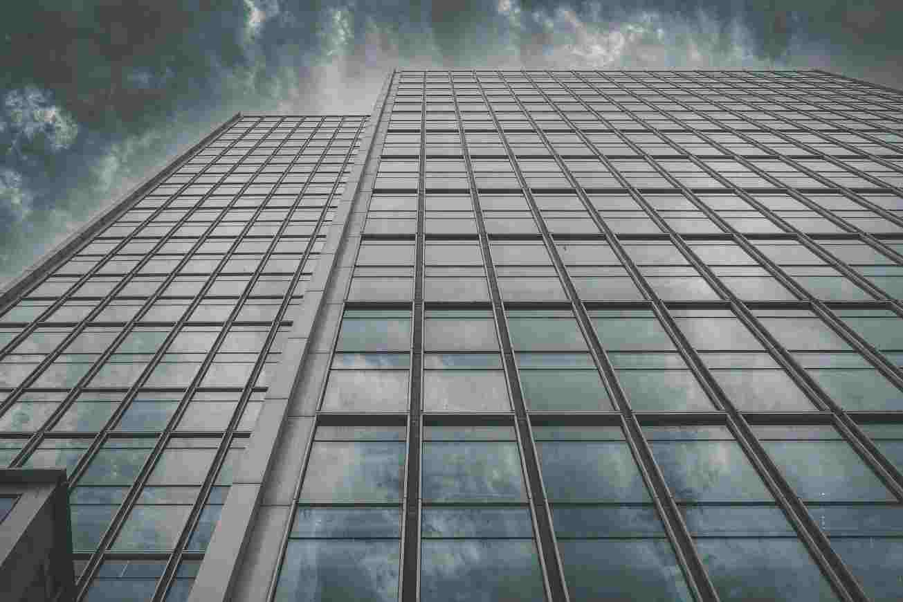 Una torre per uffici di vetro vista dal basso contro un cielo nuvoloso