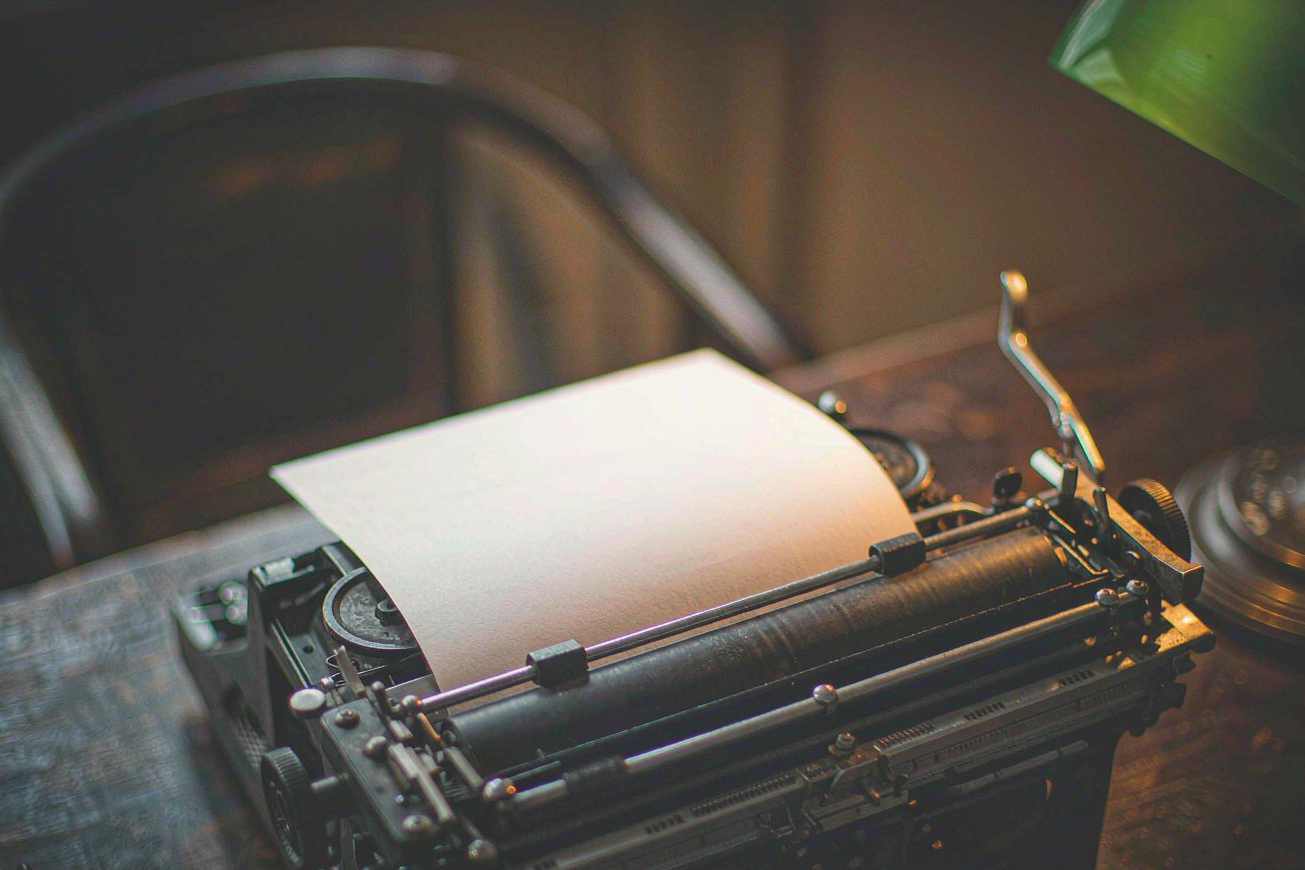 An antique mechanical typewriter holding a blank sheet of paper under a green desk lamp
