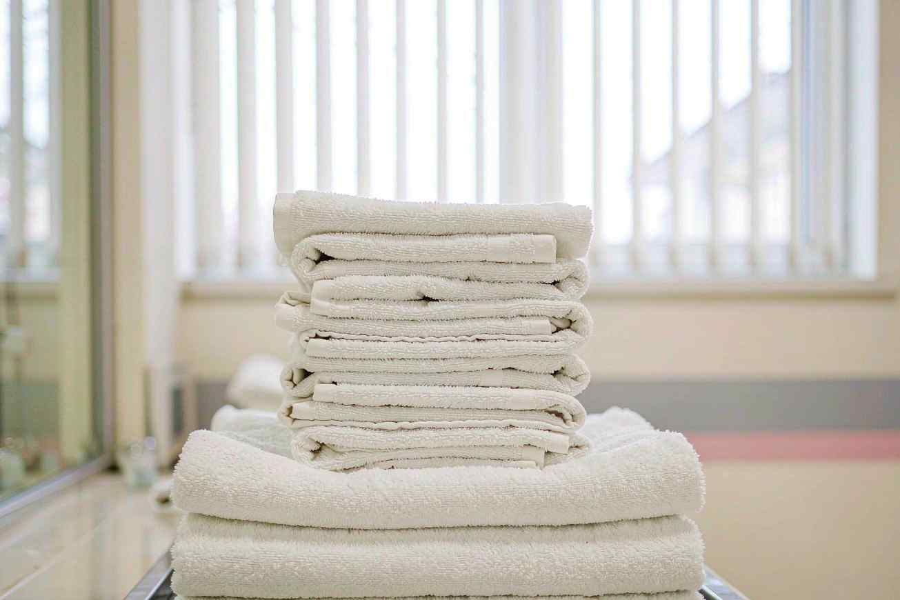 A tall stack of perfectly folded white towels on a brushed steel shelf