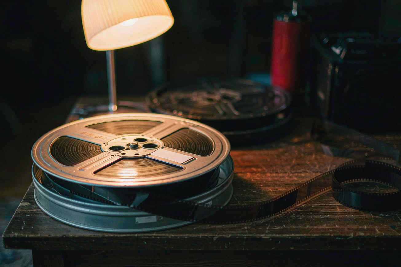 暖かなランプの下、風化した木のテーブルに置かれた古いフィルムリールと未露光のフィルム片