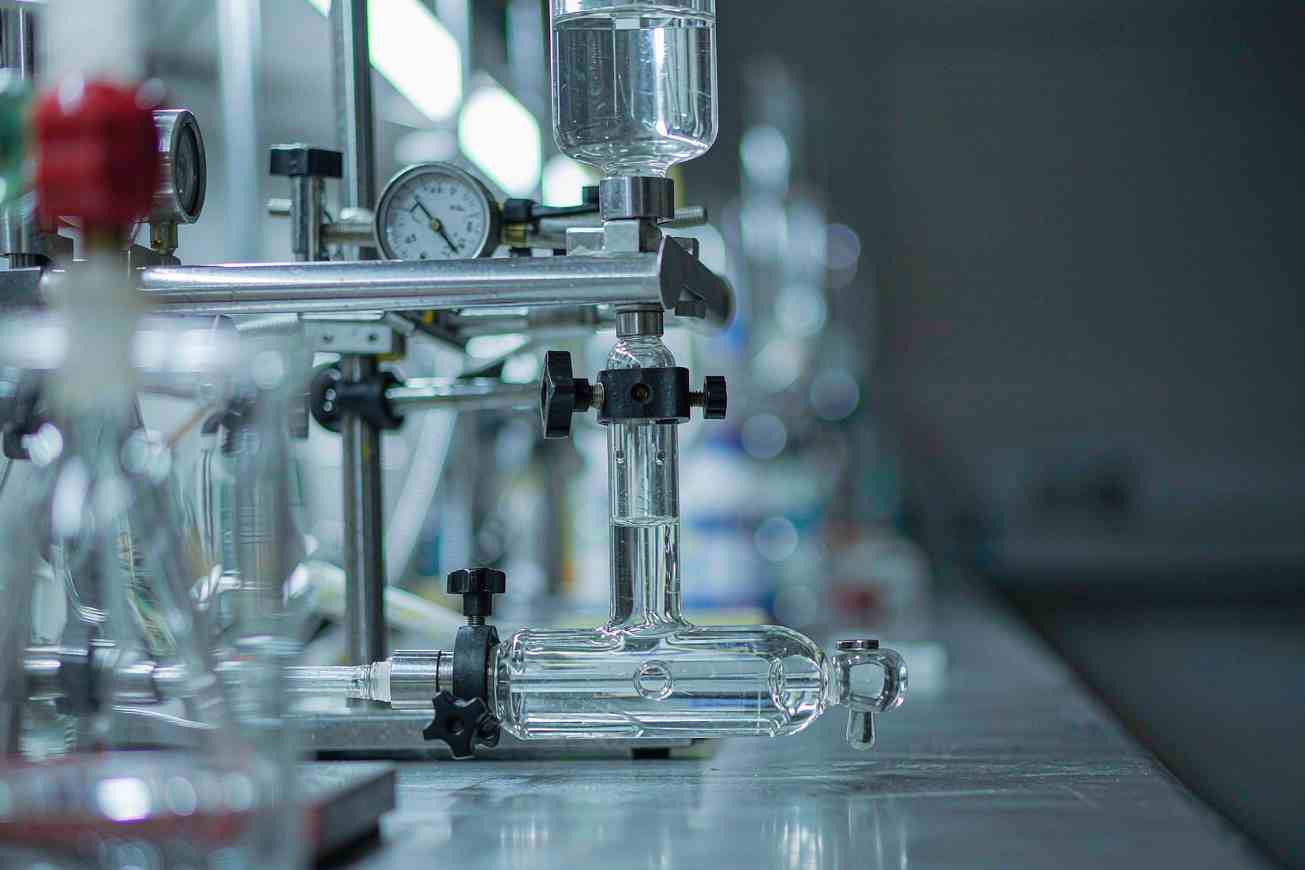 Material de laboratorio de vidrio sobre una encimera de acero inoxidable con una pantalla oscura desenfocada detrás