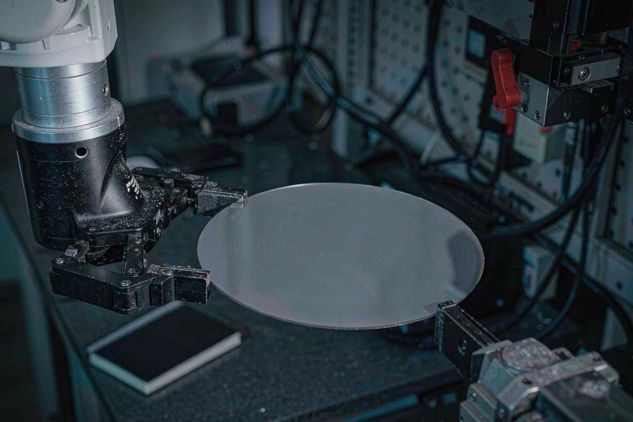 A robotic arm holding a bare silicon wafer over a dark workbench