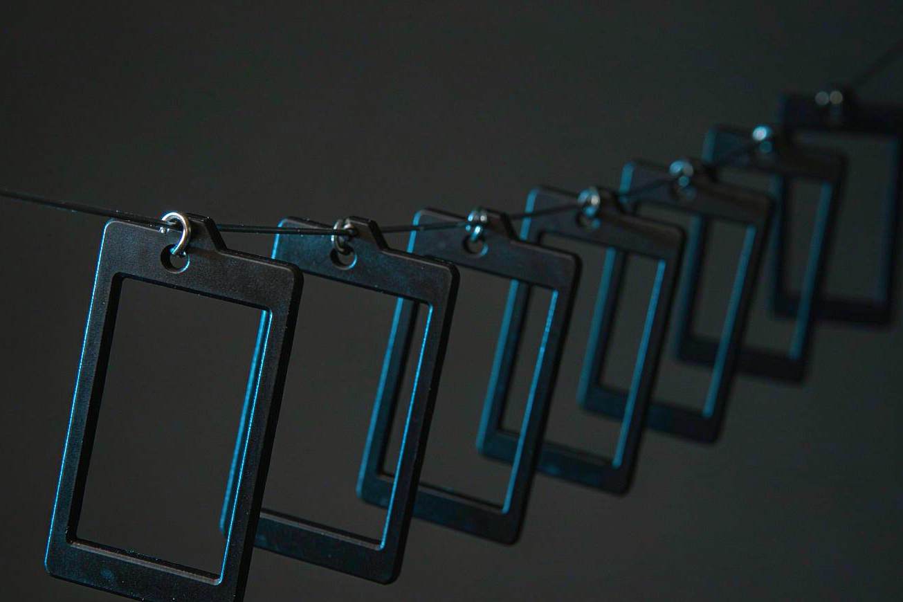 A row of blank dark film frames hanging from a thin wire against a charcoal background