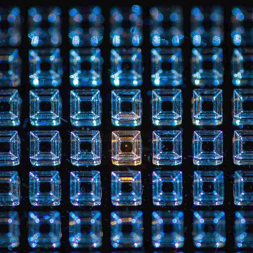 A square grid of transparent glass cells glowing cool blue with a single warm one