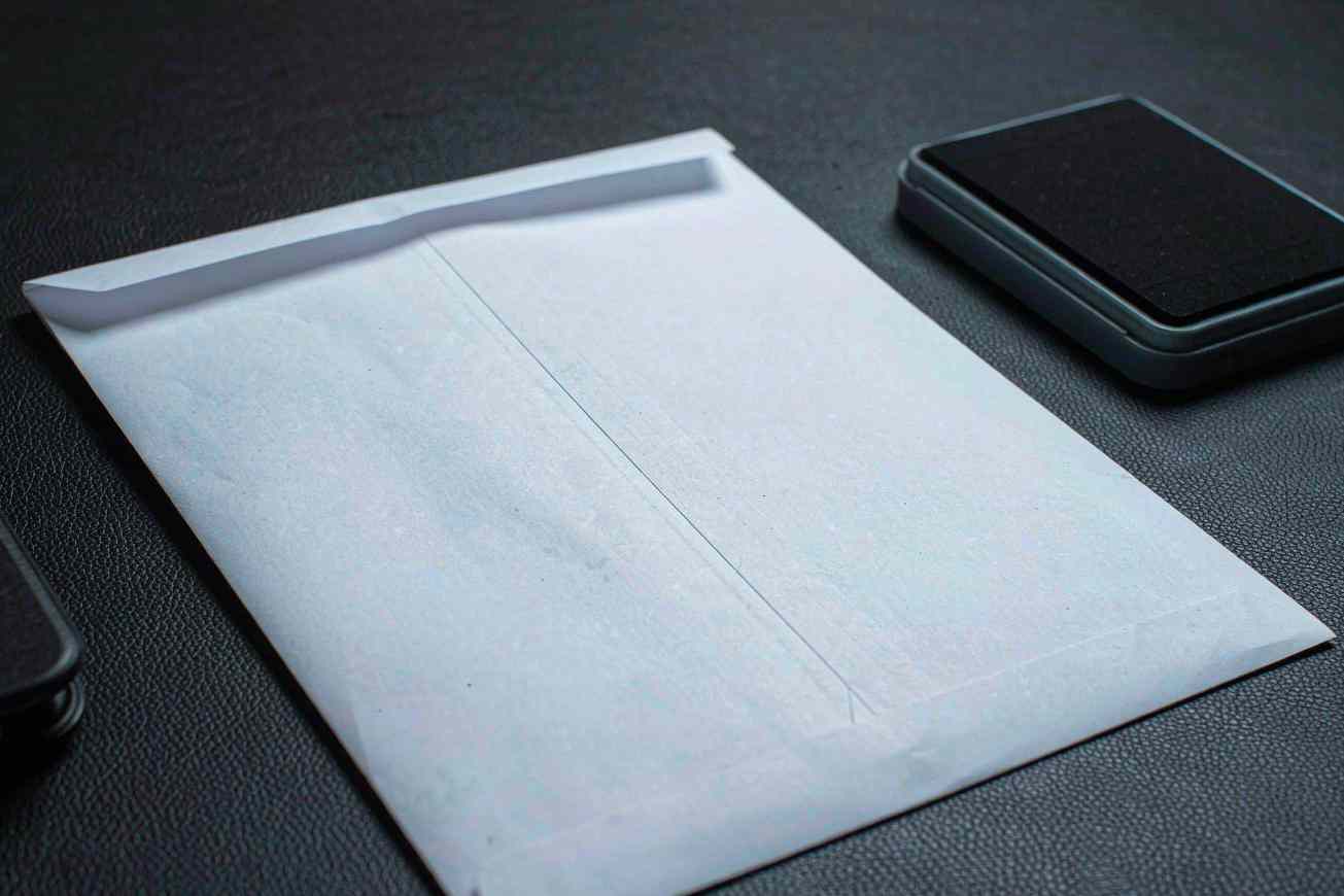 A blank white envelope beside a plain black card case on a dark textured desk