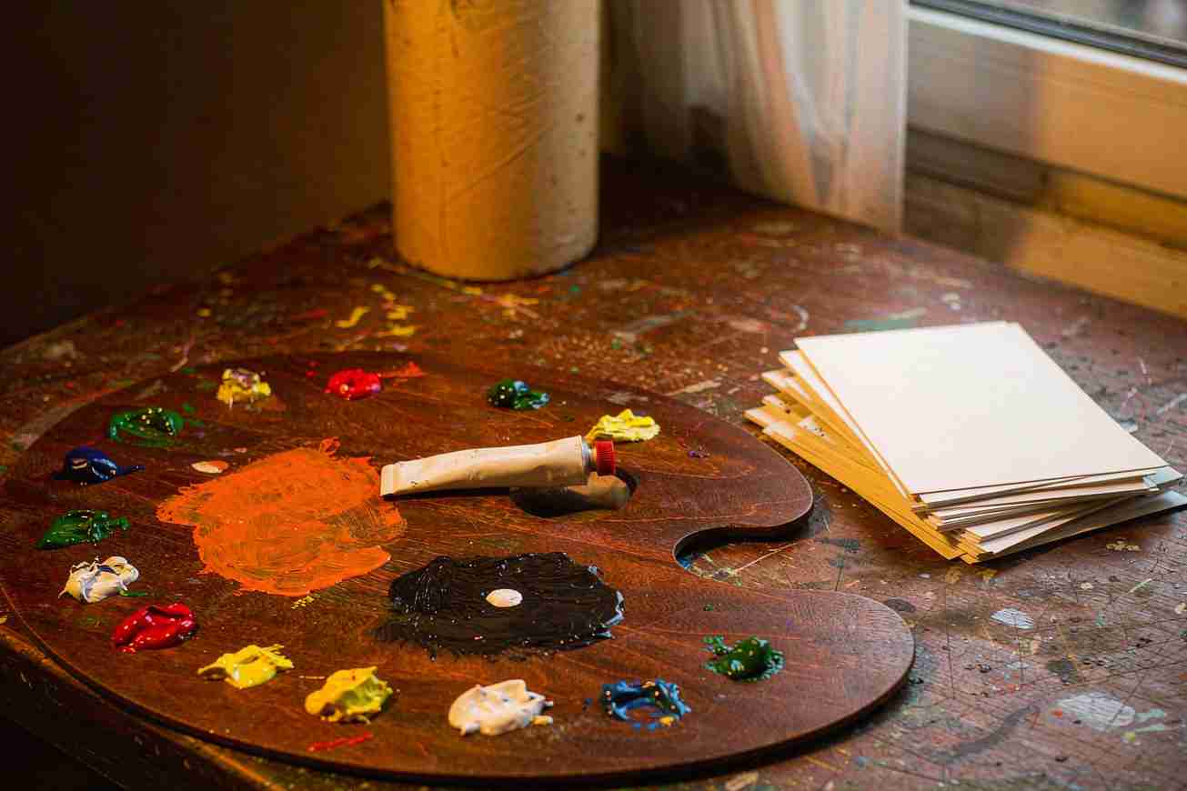 A wooden palette holds several dabs of fresh paint, with a small stack of blank cards beside it