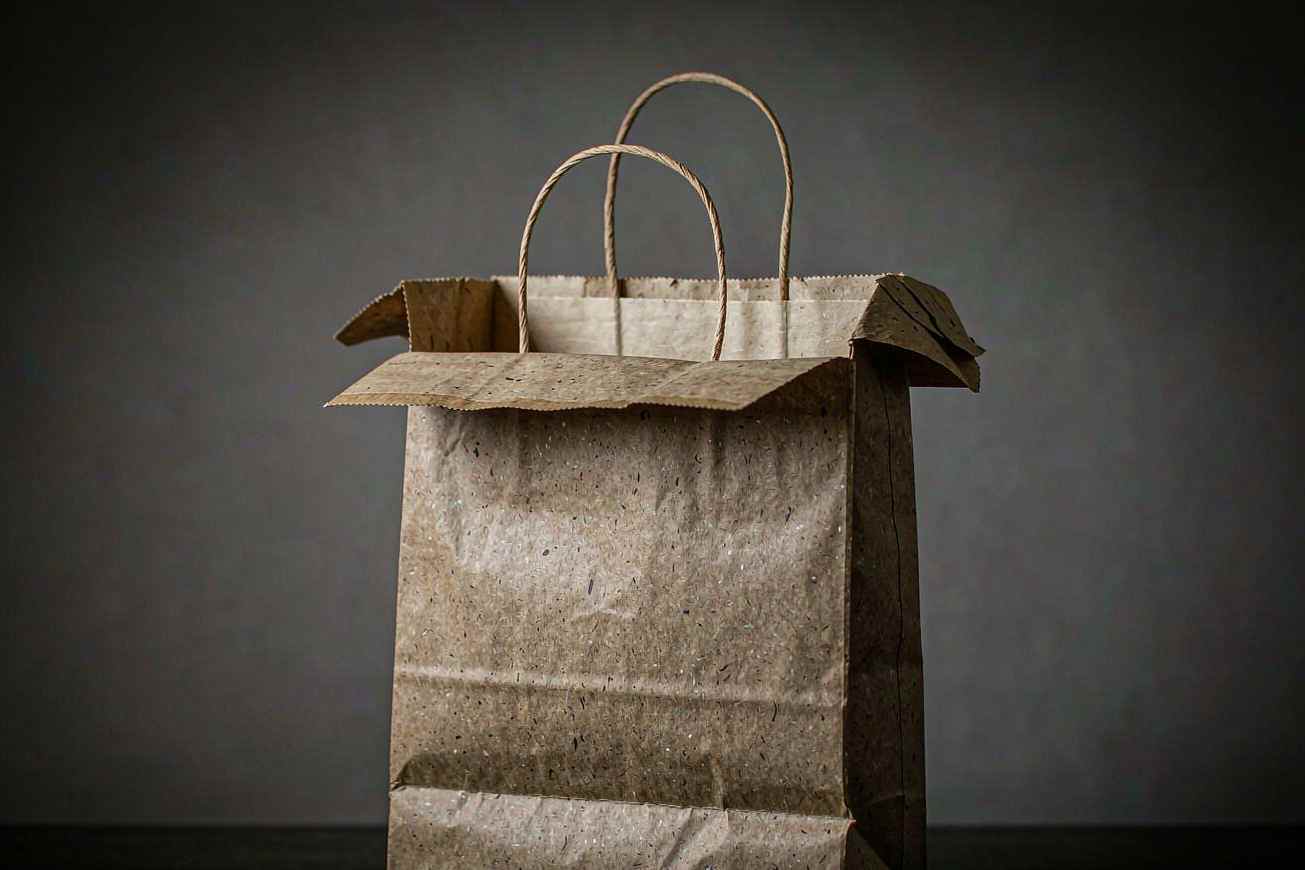 A plain unbranded brown paper shopping bag standing on a dark wooden surface
