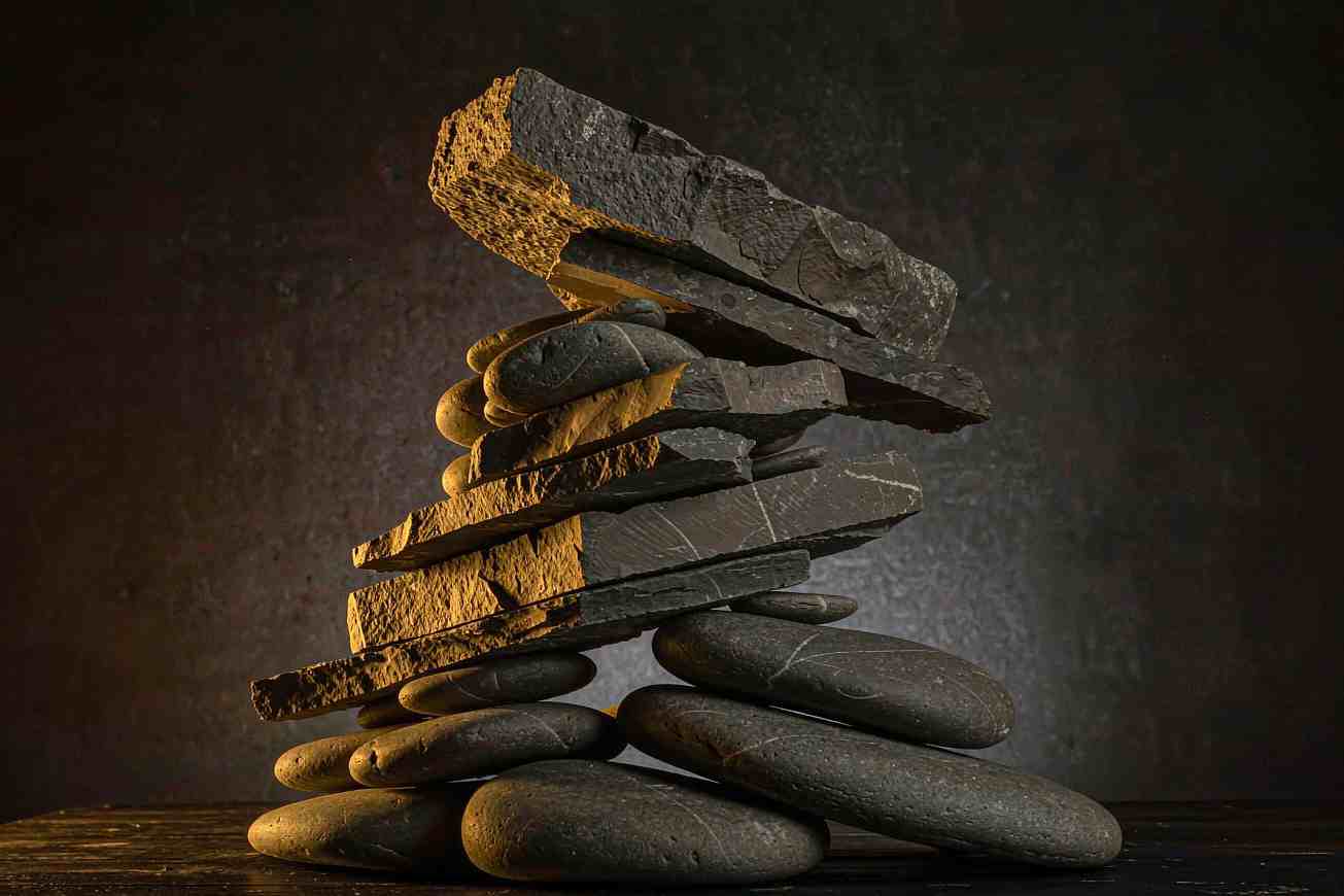 A tall stack of flat rough stone blocks balanced on a dark surface in hard light