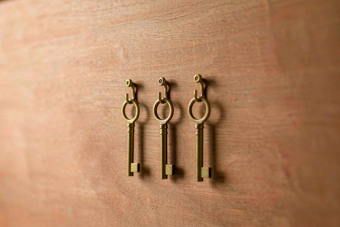 Three plain brass keys hanging from small hooks on a blank wooden board