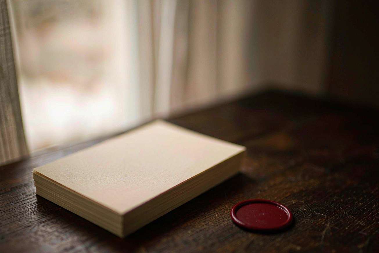 A tidy stack of blank cream cards beside a single unmarked dark red wax seal