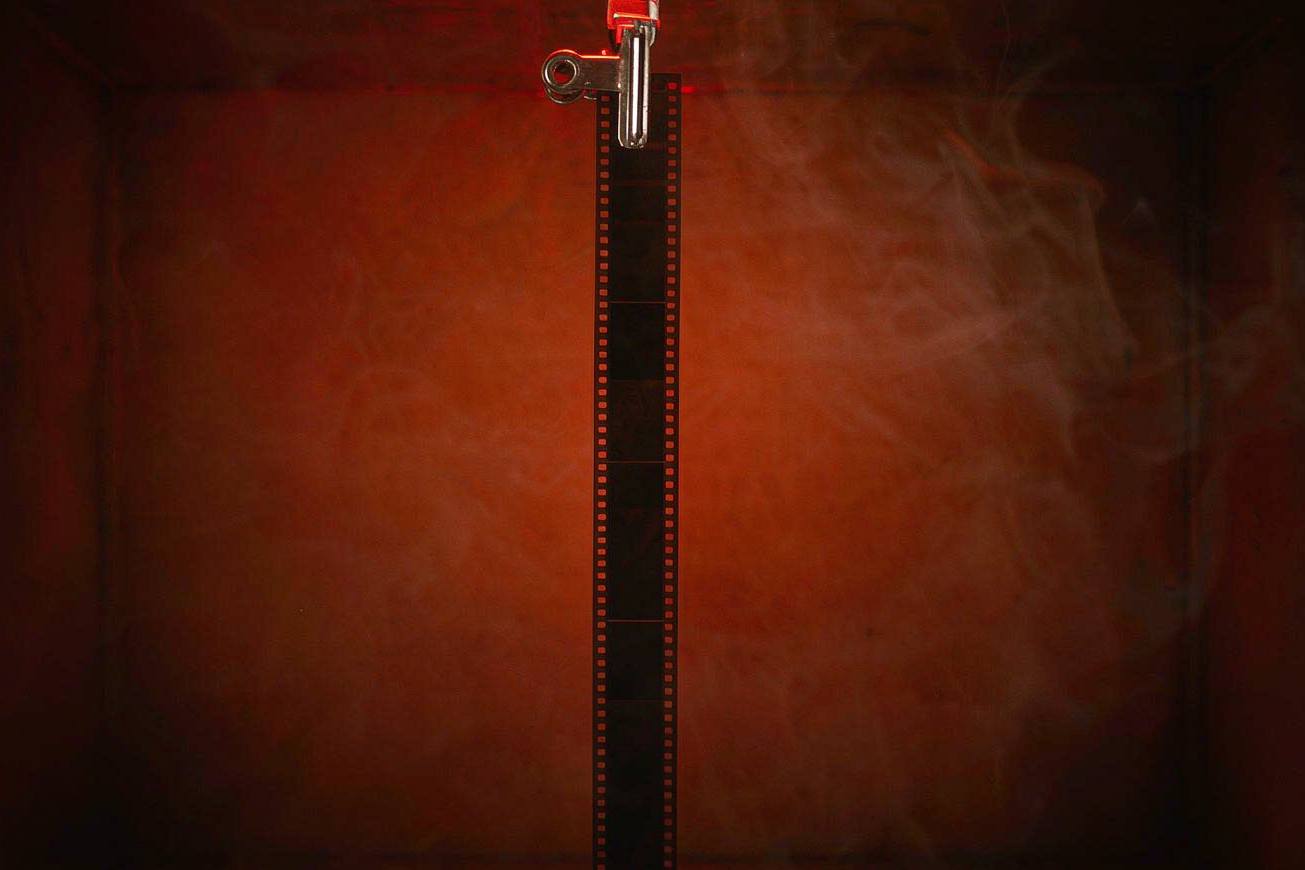 A single strip of blank unexposed film hanging from a clip in a dark red-lit darkroom