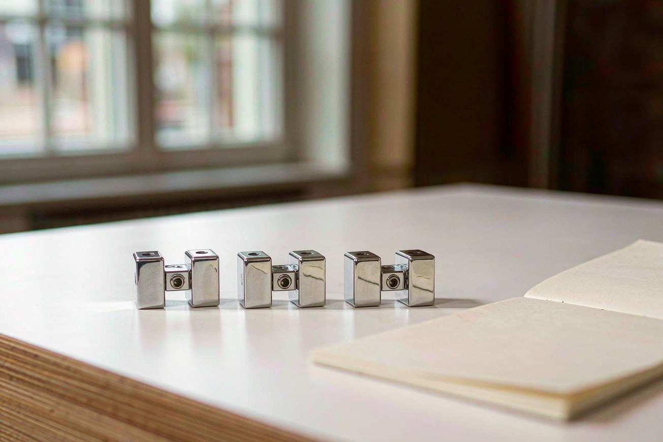 A blank lab notebook page on a light-colored woodworking bench, with three polished metal joint components side by side next to it
