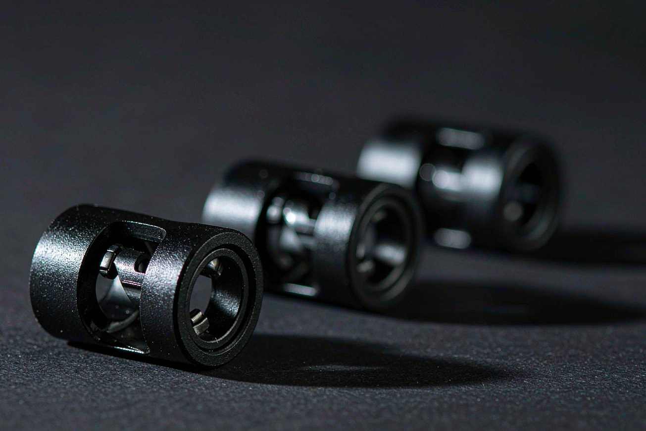Close-up of three matte black aluminium articulated finger joints on a dark grey surface