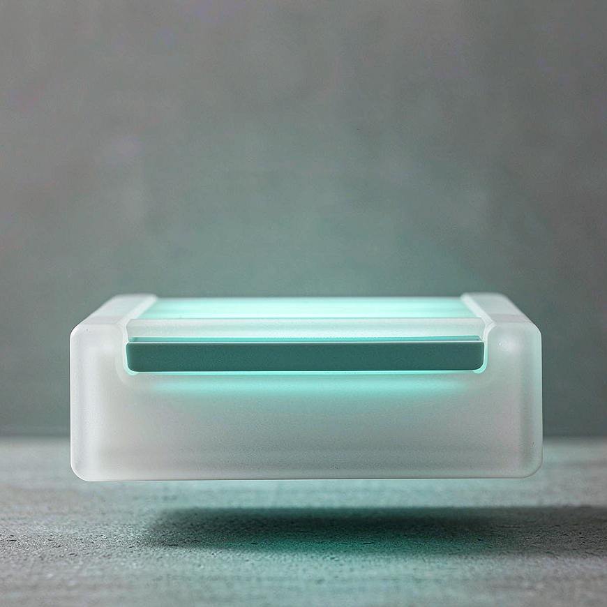 Une barre unique en verre dépoli luisant d'un éclat bleu-vert, en suspension juste au-dessus d'une surface de pierre grise unie