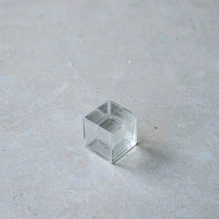 One small translucent glass cube standing alone on a pale concrete slab