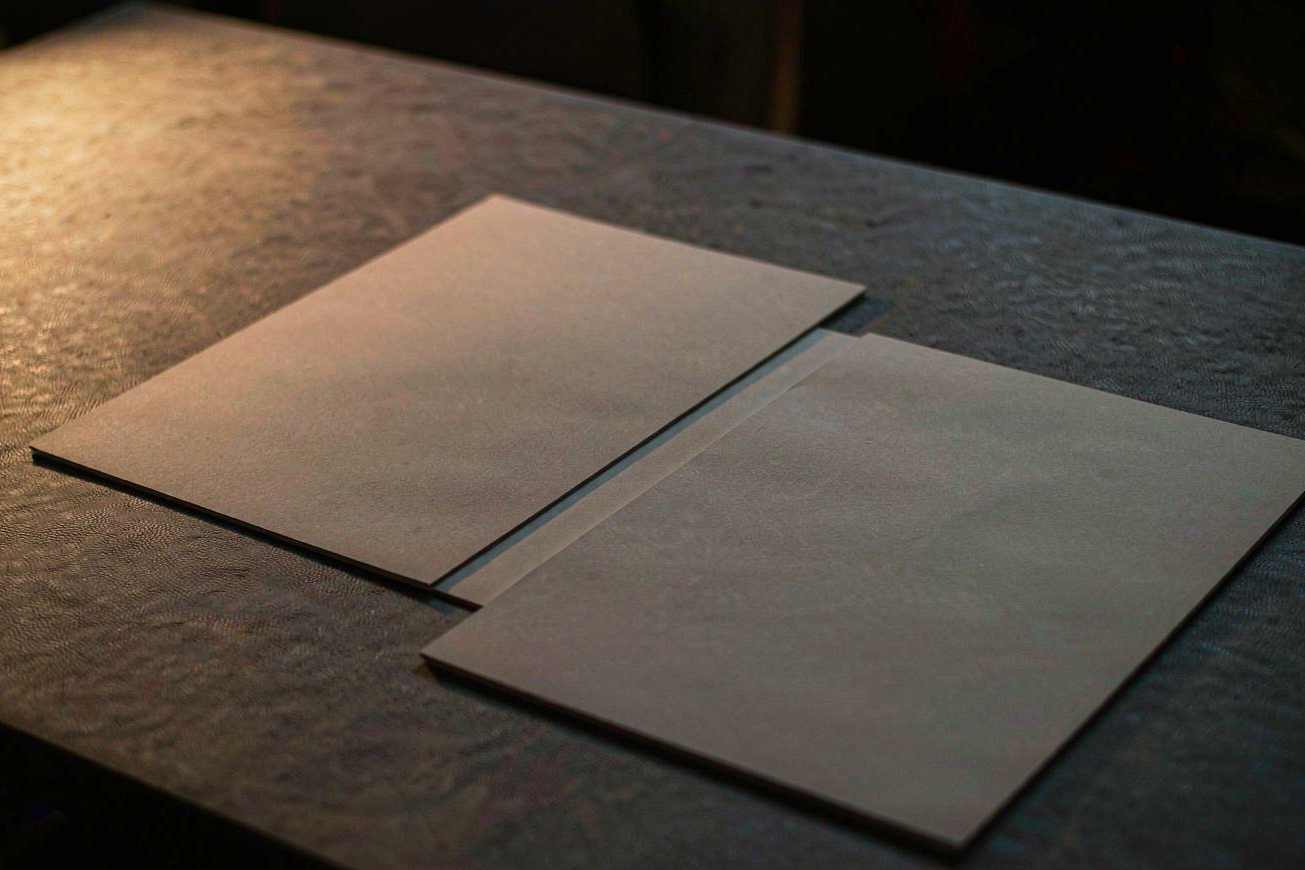 Zwei leere, unmarkierte matte Fotoabzüge, die auf einem dunkelgrauen Arbeitstisch übereinanderliegen