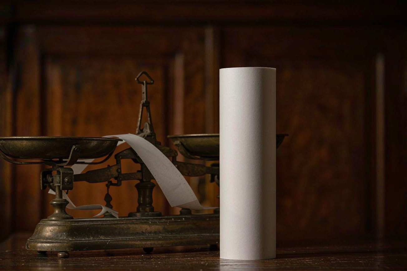 A roll of blank white paper tape beside a small brass balance scale on a dark desk
