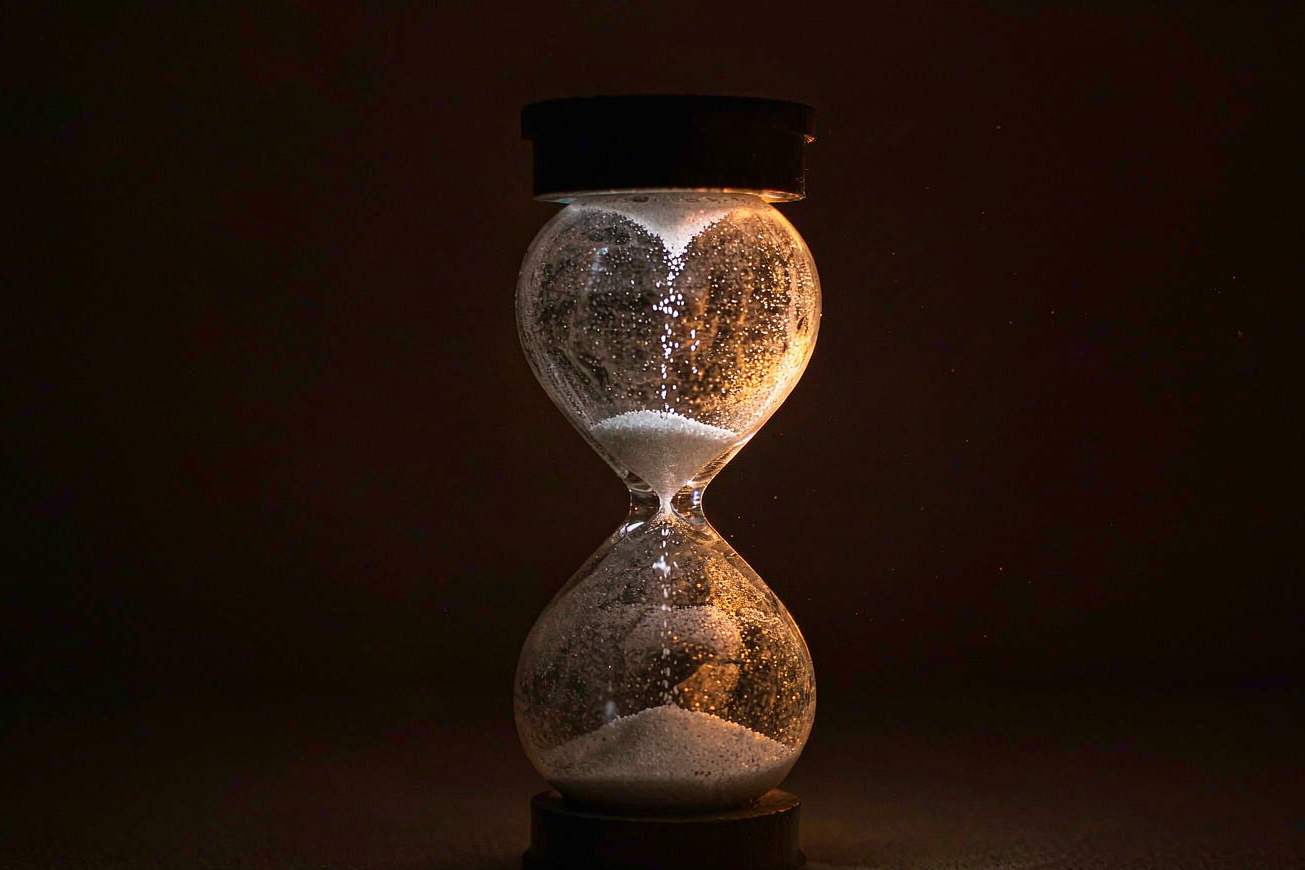 Eine einzelne leere Sanduhr aus mattiertem Glas auf dunklem Untergrund mit warmem Kantenlicht