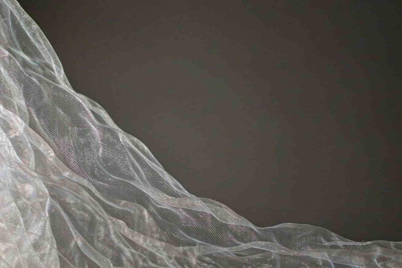The crisp edge of sheer translucent fabric against a dark seamless backdrop with no color halo