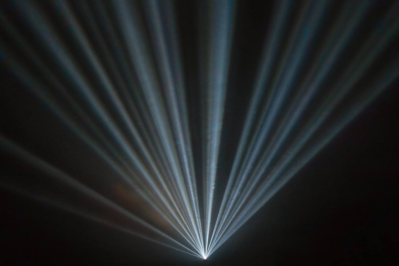 Dozens of thin parallel beams of pale blue light streaming through a dark void toward a distant point