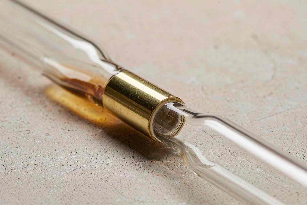 Two clear glass tubes joined end to end by a polished brass fitting with a warm amber liquid flowing through