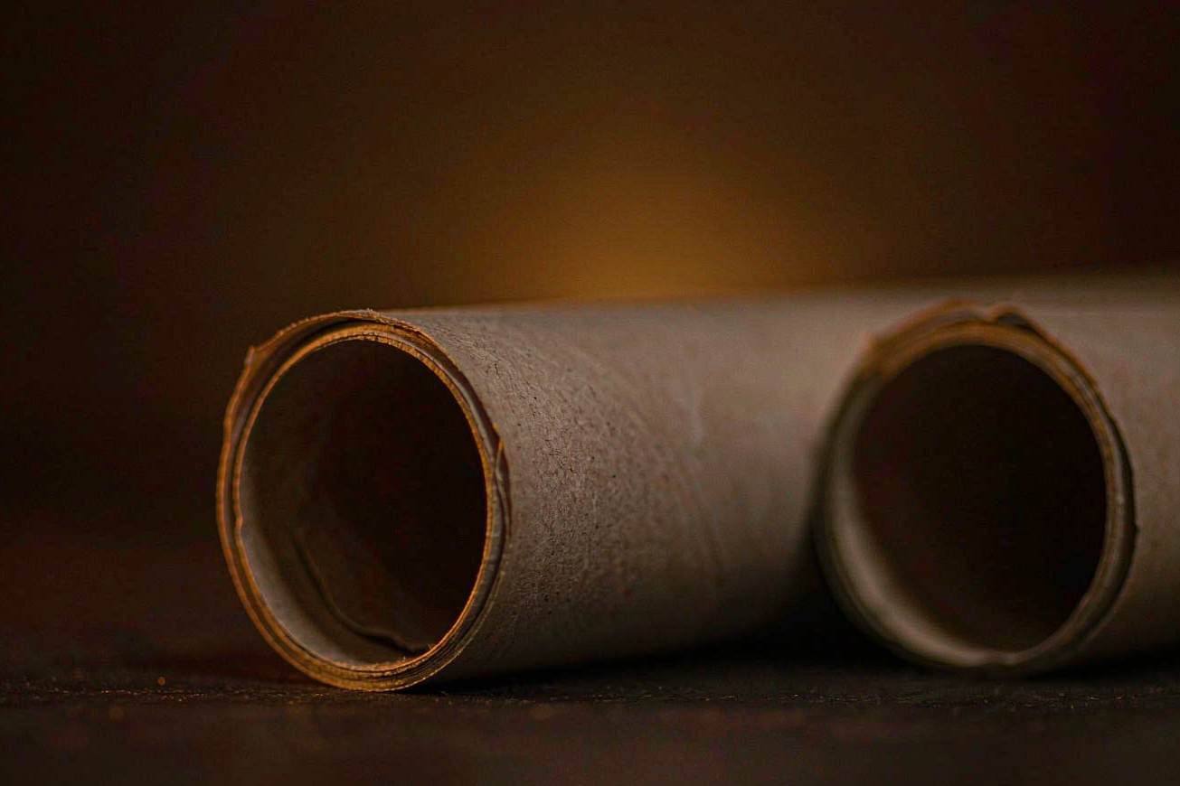 Two tightly rolled blank newsprint cylinders lying side by side on a dark surface in soft focus