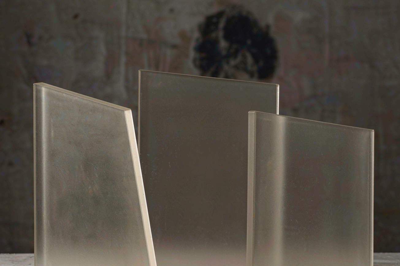 Three translucent frosted glass panes standing at slight angles on a pale stone surface, soft daylight passing through them