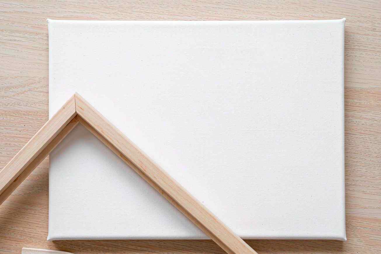 Uma folha de tela branca em branco sobre uma mesa de carvalho pálido com uma moldura fina de madeira inclinada em um ângulo e sem desenho nela