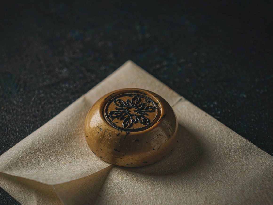A wax seal with a deep abstract floral impress resting on a folded sheet of heavy cream paper under warm light.