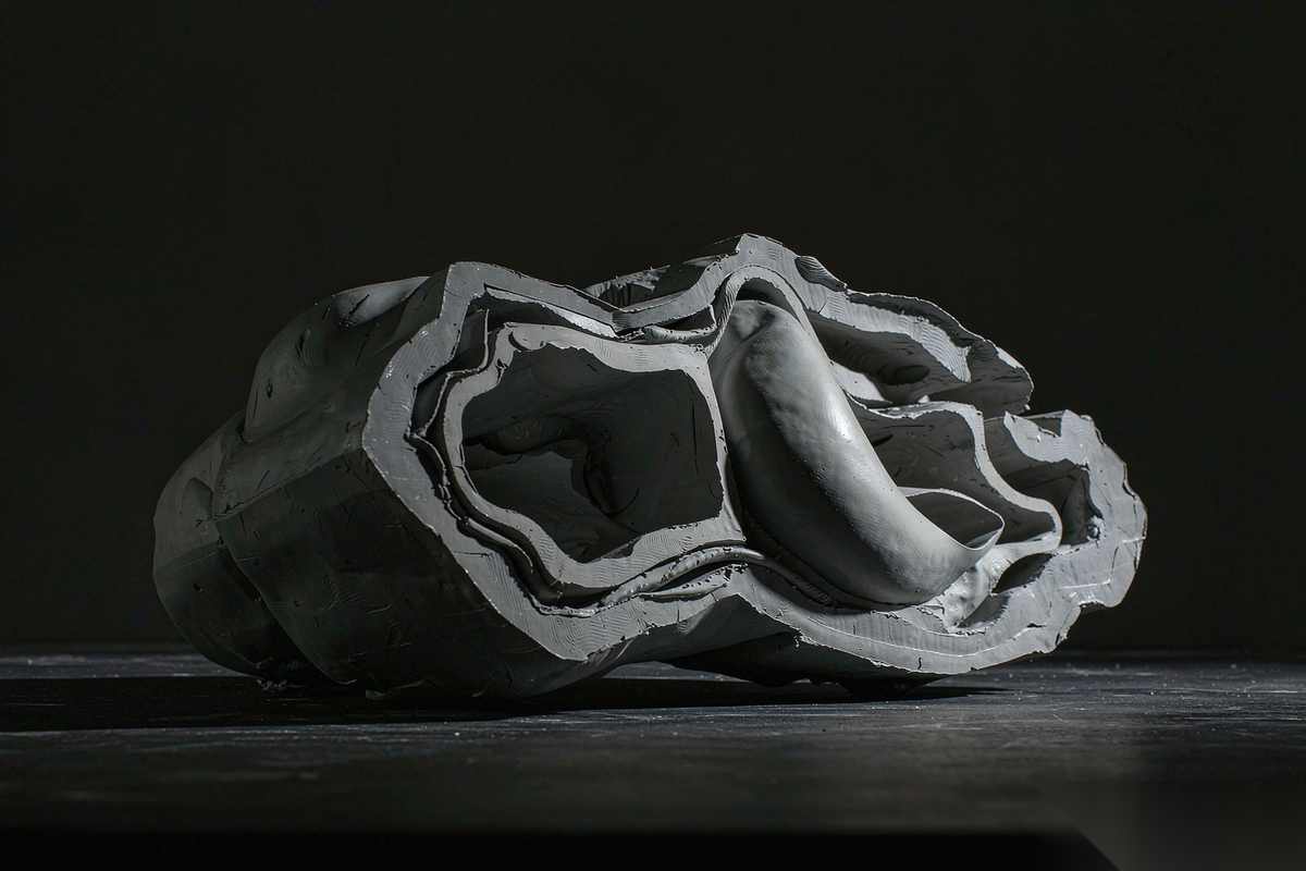 A folded fabric form floating in a dark void, its open interior and thin edges visible, lit from one side with soft rim light on the material